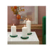 Three white candles in green holders on a white surface with a blurred indoor background.