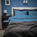 Modern bedroom with IKEA ÄNGSNEJLIKA duvet cover and pillowcases in blue geometric pattern, paired with a dark gray blanket, white headboard, and minimalist decor including wall-mounted reading lights and a black nightstand.

