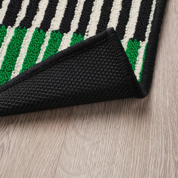 Close-up of a IKEA VÄNDPLATS Door Mat with black, white, and green stripes on a wooden floor.