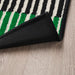 Close-up of a IKEA VÄNDPLATS Door Mat with black, white, and green stripes on a wooden floor.