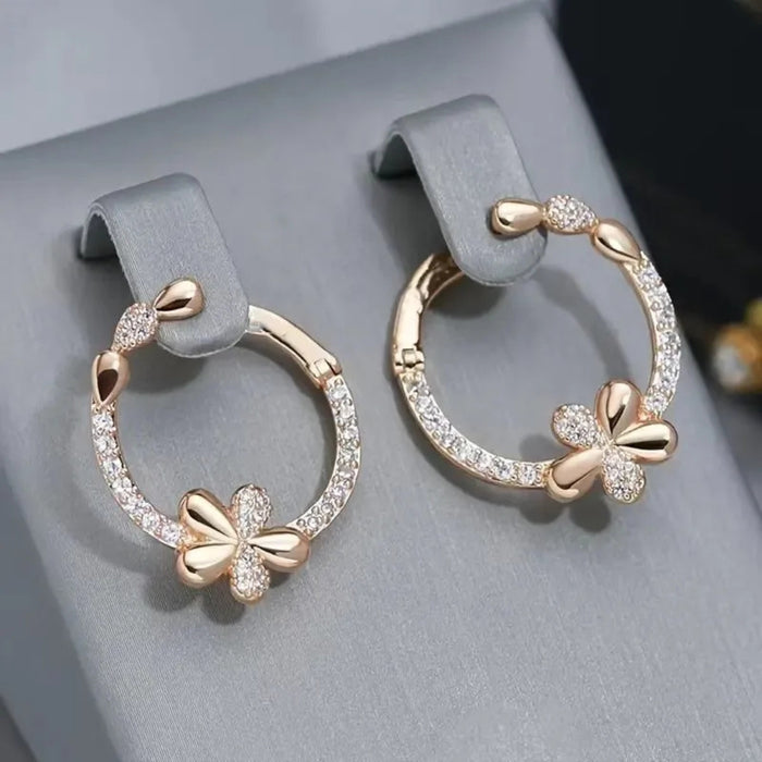 Rose gold hoop earrings with butterfly designs on a gray surface