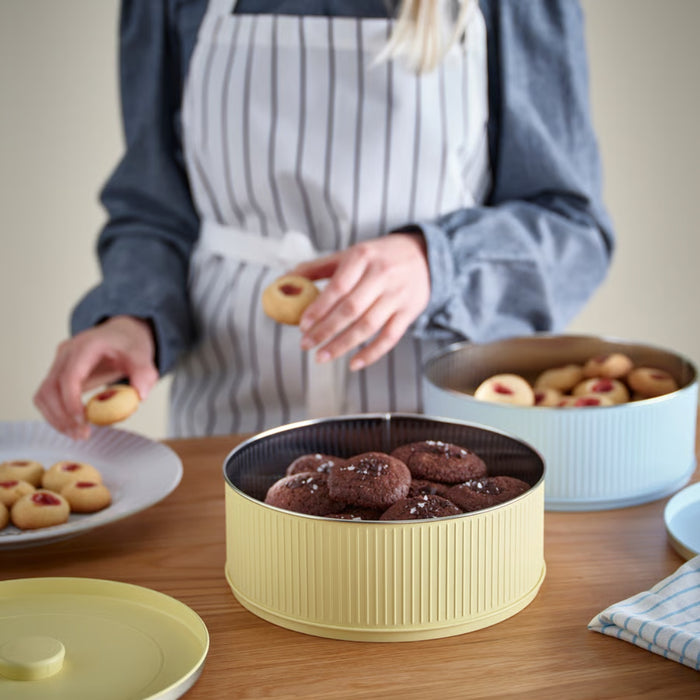 Person arranging cookies on a table with a yellow cookie tin.