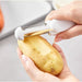 Person peeling a potato with a white peeler on a light gray background