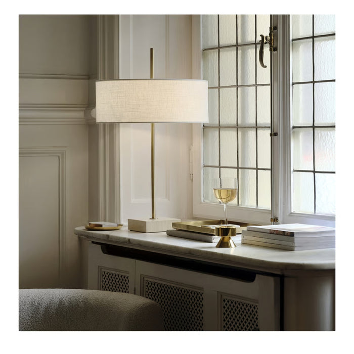 Modern interior with a lamp, books, and a glass on a table near a window.