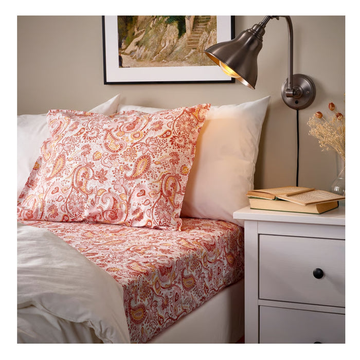 Bed with paisley patterned bedding and a nightstand with books in a bedroom setting.