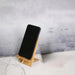 Smartphone placed vertically on a bamboo stand with charging cable inserted—clean, minimal desk setup on white surface – 1600000766929 13074717.