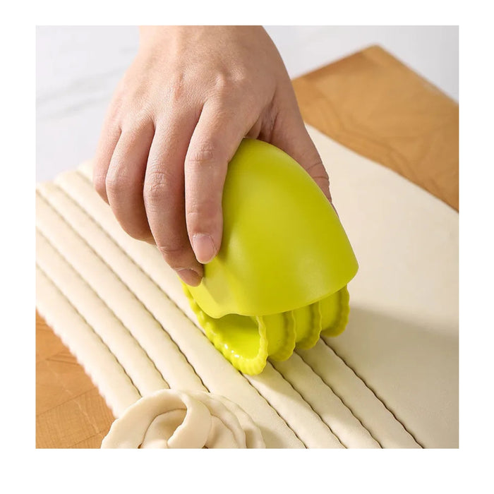 Hand using a green pasta maker to create noodles on a white background