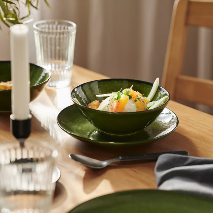 Elegant dining table setup featuring green PELARKAKTUS bowls and plates with clear glassware and candles.