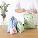 Set of colorful drawstring bags on a wooden table, including blue floral and green fruit prints – 1598445710448 14078092