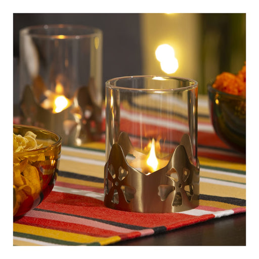 A lit candle inside the AROMATISK glass holder on a colorful striped tablecloth, creating a warm and festive glow.