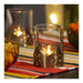 A lit candle inside the AROMATISK glass holder on a colorful striped tablecloth, creating a warm and festive glow.