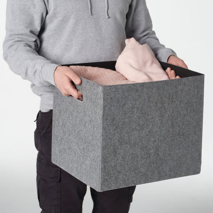 Person holding a gray storage box with clothes inside on a white background