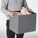 Person holding a gray storage box with clothes inside on a white background
