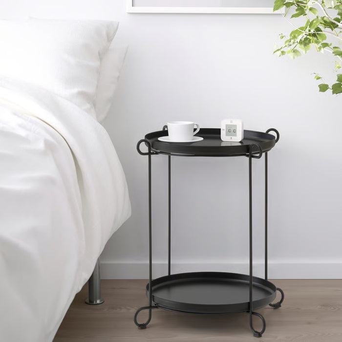 Black metal side table with a cup and small clock next to a bed