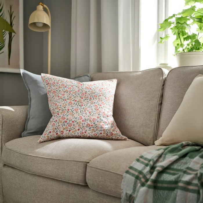 GULLNATTLJUS cushion cover, white/floral, 50x50 cm. Styled on beige sofa with green throw and pastel cushions. Adds soft, botanical charm to living space – 90598702.