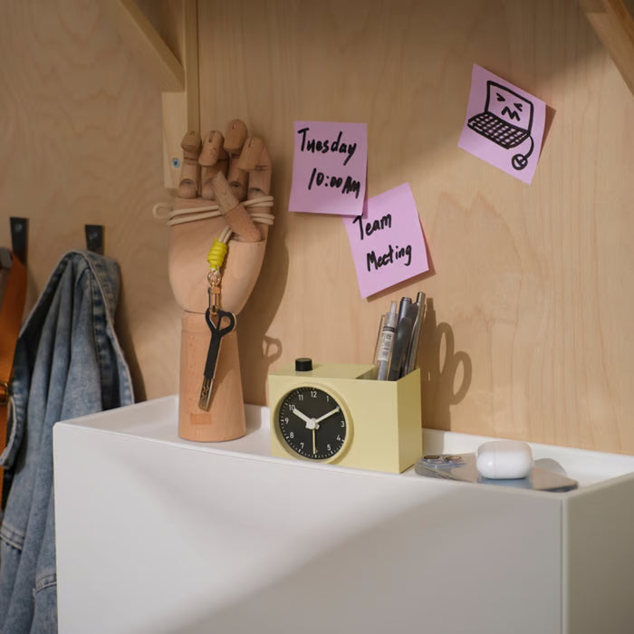 Desk setup with a clock, stationery holder, and sticky notes on a wooden wall.