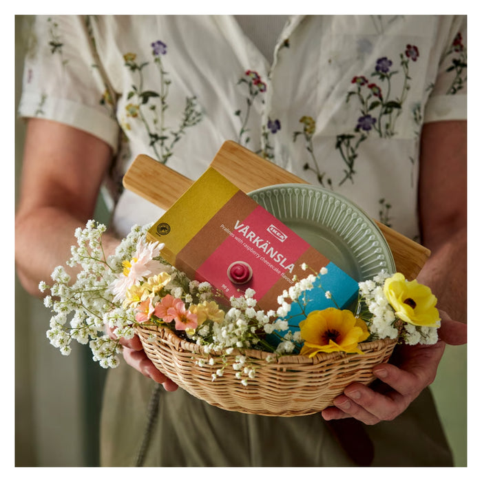 Person holding a basket with flowers and a box labeled 'Värkånsla'.
