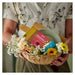 Person holding a basket with flowers and a box labeled 'Värkånsla'.