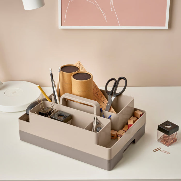 Desk organizer with office supplies on a white surface, framed artwork in the background.