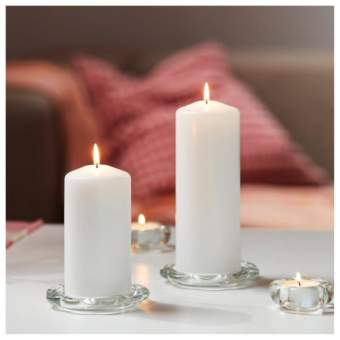 Two white candles on a table with a blurred background of a couch and pillows.