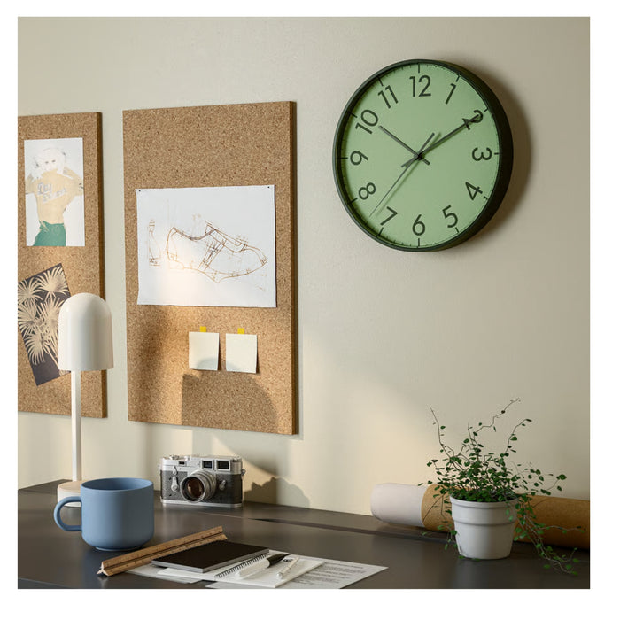 Wall clock on a wall with cork boards and a desk setup.