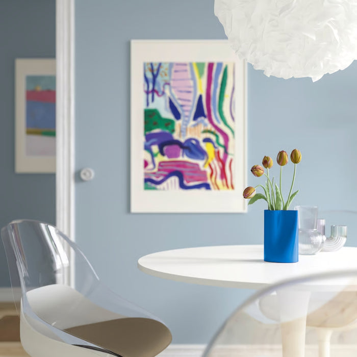 Modern dining room with a round table, clear chair, and colorful abstract art on the wall.