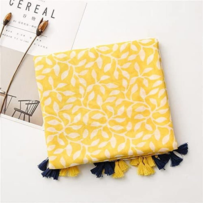 Digital Shoppy shawl scarf – folded yellow leaf-patterned scarf with blue-yellow tassels placed over minimalist magazine

