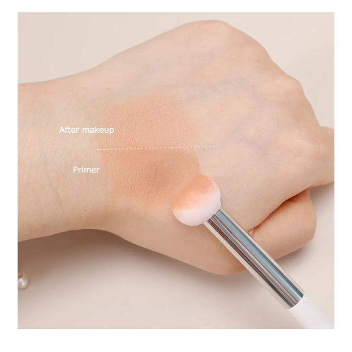 Hand applying primer and makeup with a brush on a neutral background