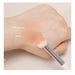 Hand applying primer and makeup with a brush on a neutral background