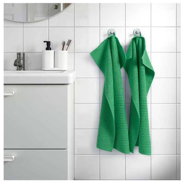 Green towels hanging on a towel rack in a bathroom with white tiles.