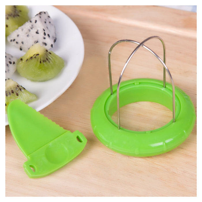 A green plastic fruit slicer with a metal wire loop and a matching green plastic blade, shown on a light wood surface next to a plate of sliced kiwi and dragon fruit.