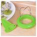 A green plastic fruit slicer with a metal wire loop and a matching green plastic blade, shown on a light wood surface next to a plate of sliced kiwi and dragon fruit.