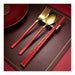 Gold and red cutlery set on a brown placemat with a red plate in the background.