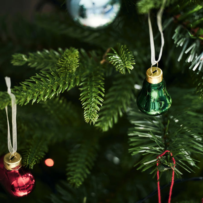 Close-up of dark green artificial pine needles and a small green bell-shaped Christmas ornament.