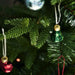 Close-up of dark green artificial pine needles and a small green bell-shaped Christmas ornament.