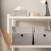 White shelving unit with neatly organized storage boxes, featuring IKEA KUGGIS light grey storage solutions, a lamp, headphones, and decorative elements—ideal for home organization and modern interior decor.- 20599149