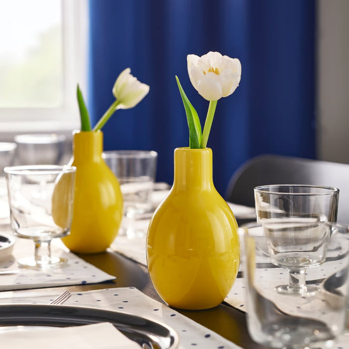 Yellow vases with white tulips on a dining table with blue curtains in the background