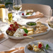 Table setting with a platter of assorted cheeses, crackers, and fruits with wine glasses.