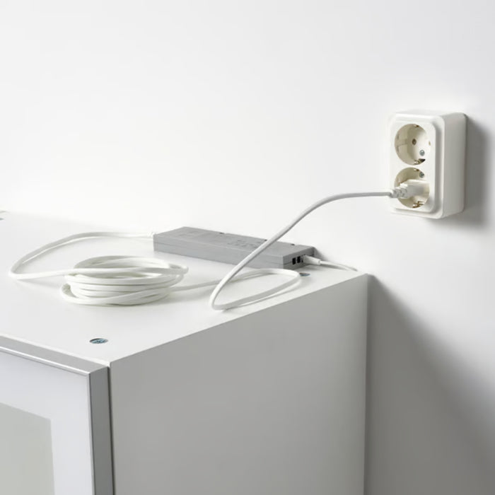 FÖRNIMMA power supply cord, 3.5 m (138"), white – coiled cord placed on a white cabinet, plugged into a dual wall socket. Ideal for connecting up to 10 integrated lamps – 50446876.