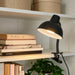 Black clamp lamp on a shelf with books and a plant