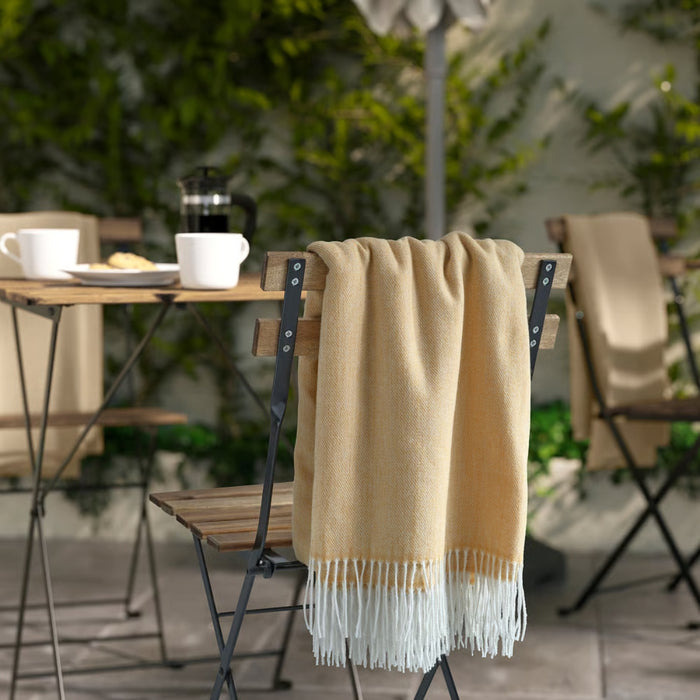 Beige throw blanket draped over a chair with a blurred outdoor setting