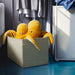 Two yellow plush octopuses in a patterned box in a laundry room.