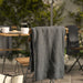 DAGGKÅPOR throw, dark grey, 130x170 cm. Draped over outdoor chair in patio setting with coffee mugs and French press on table – adds cosy touch to garden mornings – 50598643.