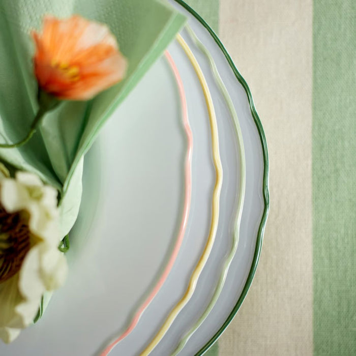  Stack of UPPLAGA plates with pastel rims layered concentrically, topped with green napkin and floral accents