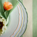  Stack of UPPLAGA plates with pastel rims layered concentrically, topped with green napkin and floral accents