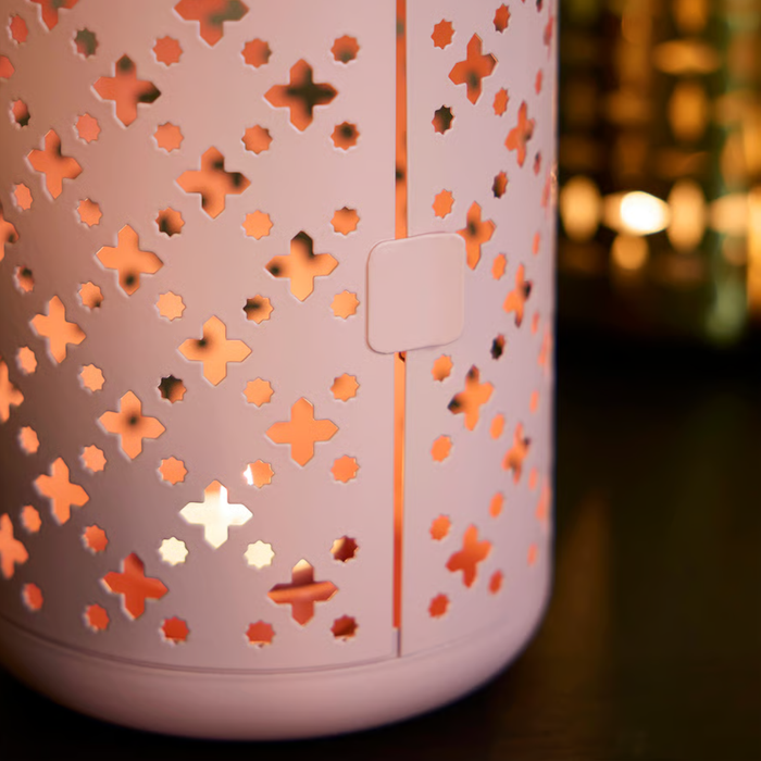 Pink lantern glowing warmly through decorative cutouts, casting patterned light in a dimly lit room.