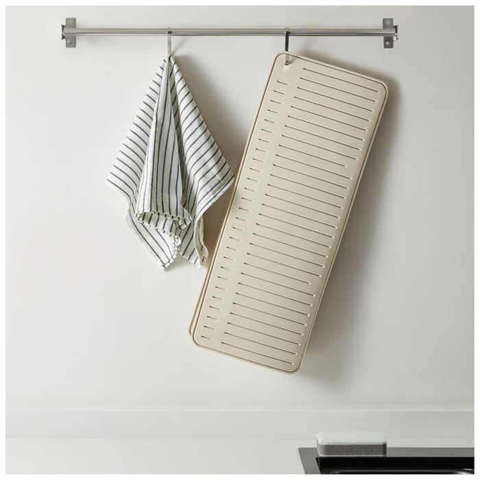 Beige bath mat with slats hanging on a towel rack against a white wall.