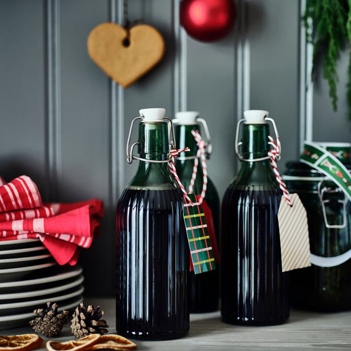 Three dark bottles with metal lids on a wooden surface, with decorative elements in the background.