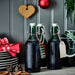 Three dark bottles with metal lids on a wooden surface, with decorative elements in the background.