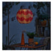 Decorative paper lantern hanging above a table with plants and a chair in a nighttime outdoor setting.